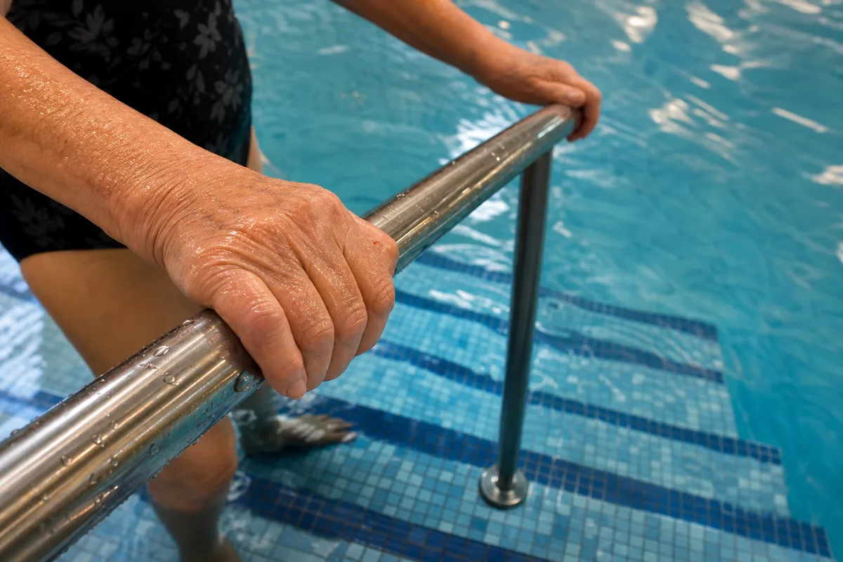 Mains d&rsquo;une personne âgée agrippant la rampe en inox à l&rsquo;entrée du bassin